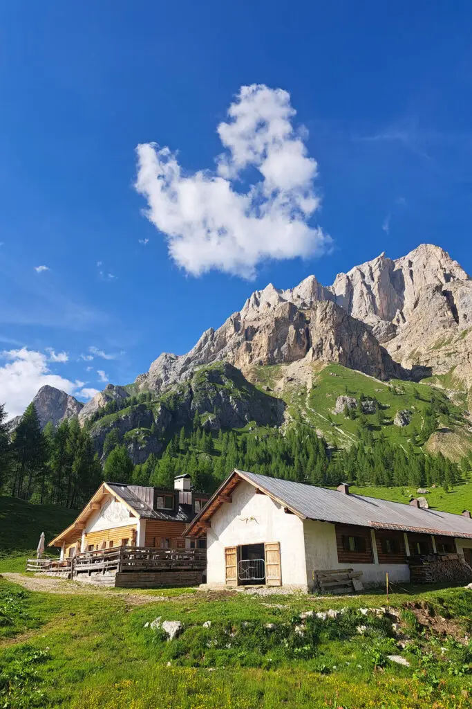 Malga tradizionale ai piedi della Marmolada, Val di Fassa, con cielo blu e nuvole pittoresche